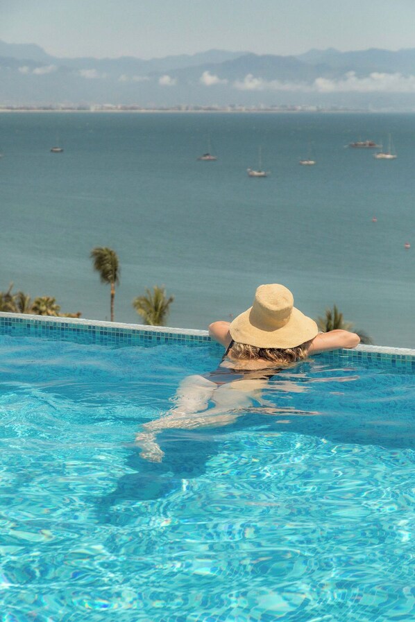Una persona relajándose en una piscina con vistas al océano y barcos.