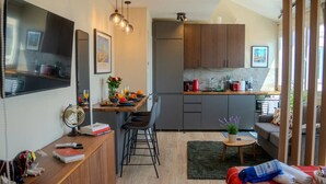 En kompakt opholdsstue med et tekøkken, spiseplads og siddeområde med sofa og lille bord.