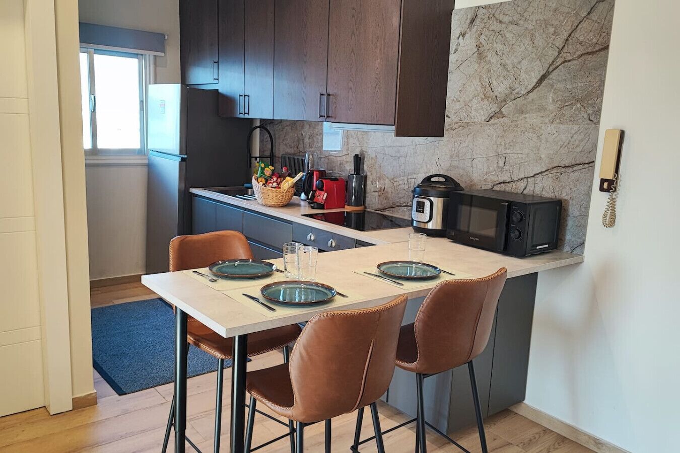 A compact kitchen with a dining area, equipped with a microwave, kettle, and a small refrigerator.