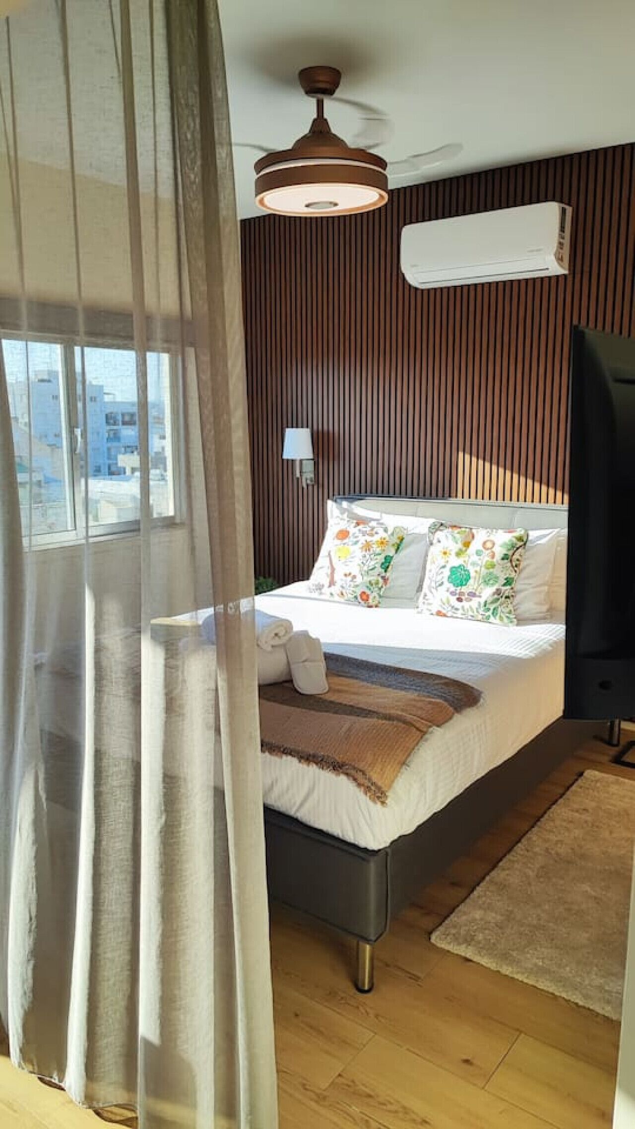 Een slaapkamer met een bed, een bedlamp, een plafondventilator en een raam met gordijnen.
