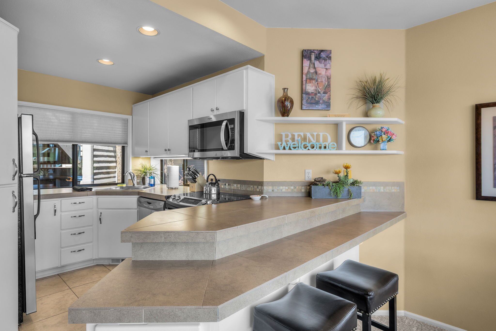 Una cocina moderna con una isla central, armarios blancos, un microondas de acero inoxidable y un cartel que dice 'REND welcome'.