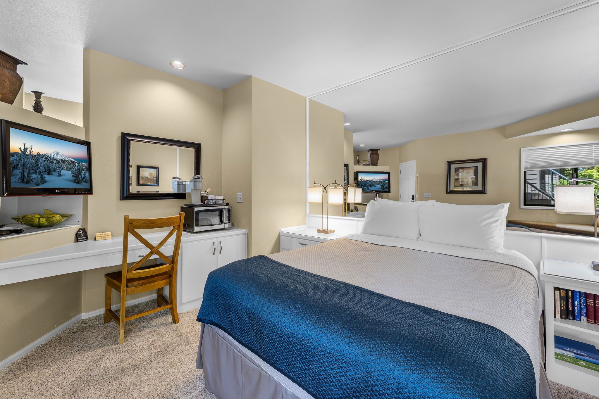 A hotel room with a bed, desk, chair, TV, and a bookshelf.