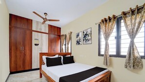Une chambre avec un lit en bois, un ventilateur de plafond, une armoire et une fenêtre avec des rideaux.