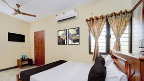 Une chambre d’hôtel avec un lit, un bureau, une chaise, une télévision et une fenêtre avec des rideaux.