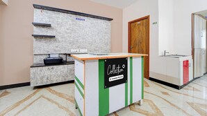 Un comptoir d’accueil avec un panneau indiquant qu’il s’agit d’un point de collecte desservi par l’entreprise, un espace d’accueil avec une porte en bois et un sol carrelé.