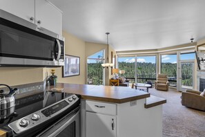 Eine moderne Küche mit Einbauherd, Mikrowelle und Backofen. Ein Essbereich bietet Blick auf einen Wald durch große Fenster.