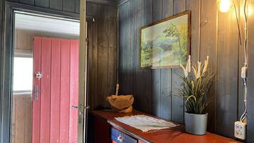 A wooden interior with a red door, a framed painting, a plant, and a light fixture.
