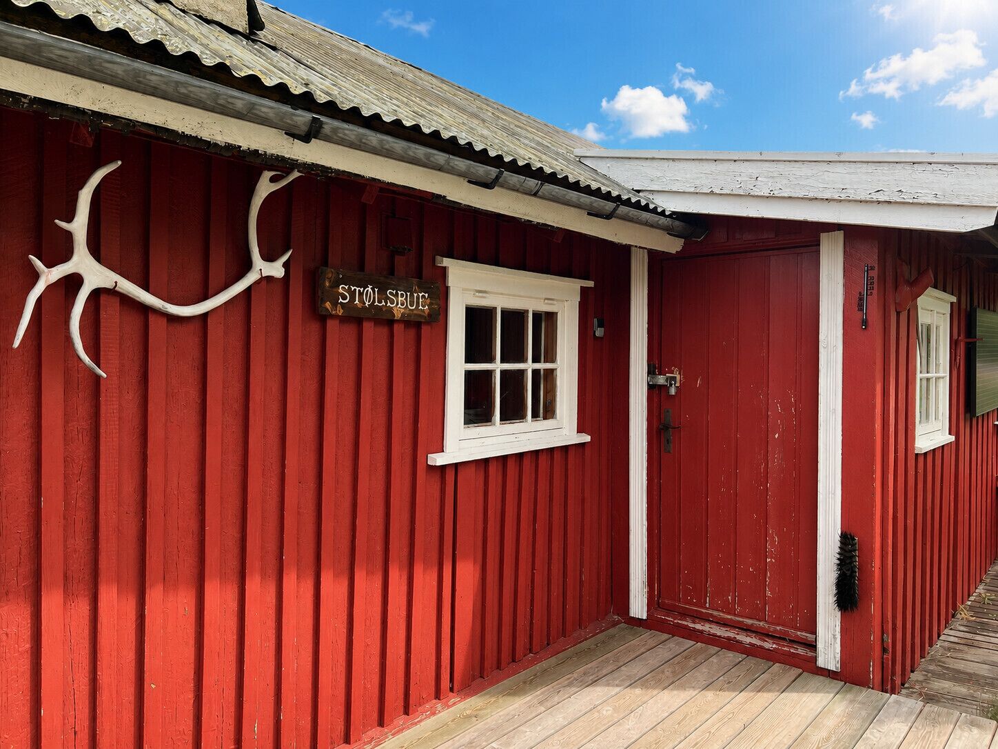 Un edificio rojo con puerta y ventana blancas, un letrero que dice 'STOLSBUE' y una terraza de madera.