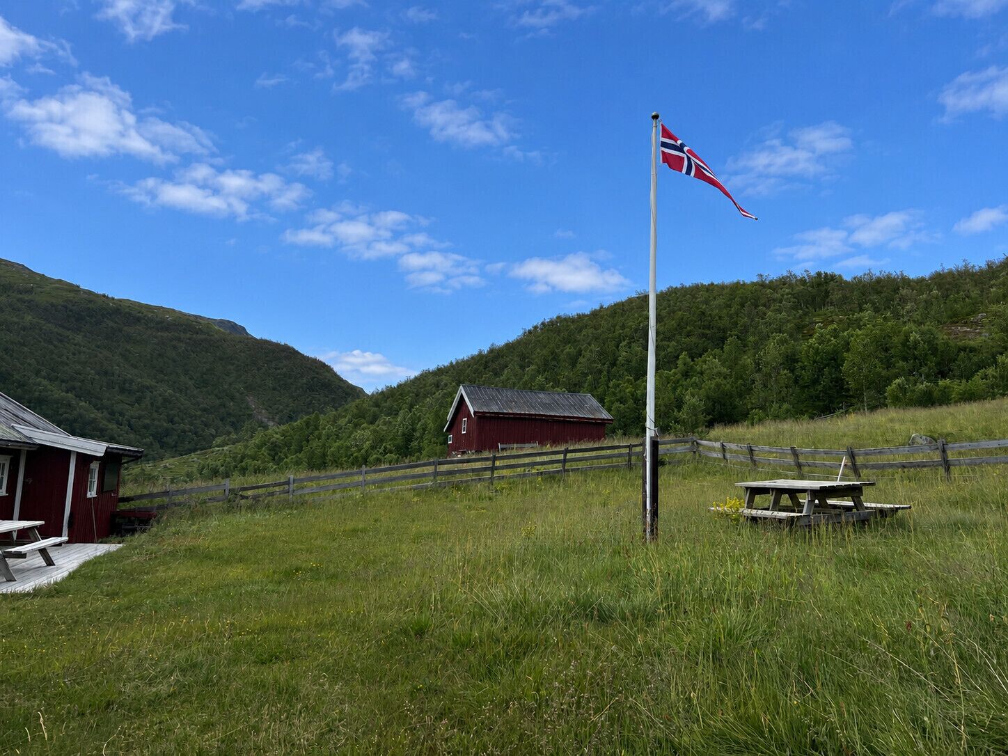 Paisaje rural con un granero rojo, una mesa de picnic y un asta con una bandera.