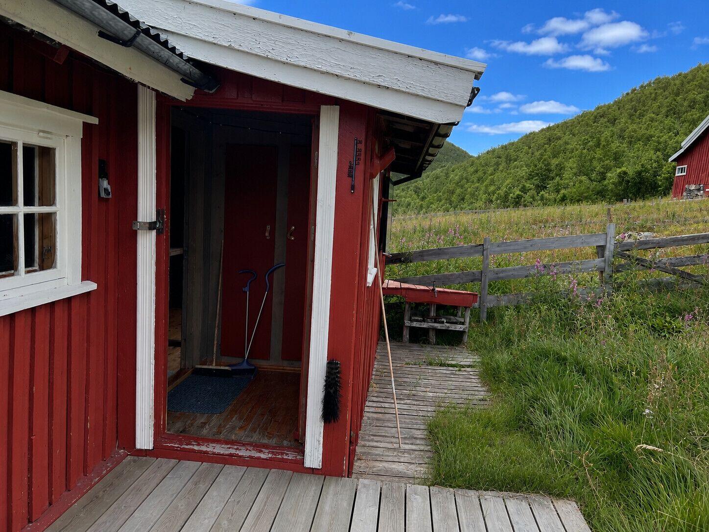 A red wooden building with a wooden deck leading to a door.