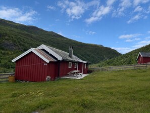 Ein rotes Bauernhaus mit Schornstein, einem Picknicktisch und einem grünen Feld im Vordergrund.