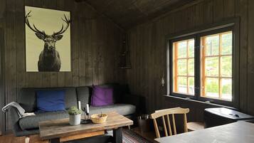Una habitación acogedora con techo de madera, un sofá con cojines, una mesa con una cesta, una silla y una ventana con vistas.