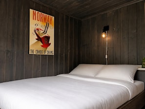 Ein Zimmer mit einem Bett, Holzwänden, einem Norwegen-Plakat und einer Wandleuchte.