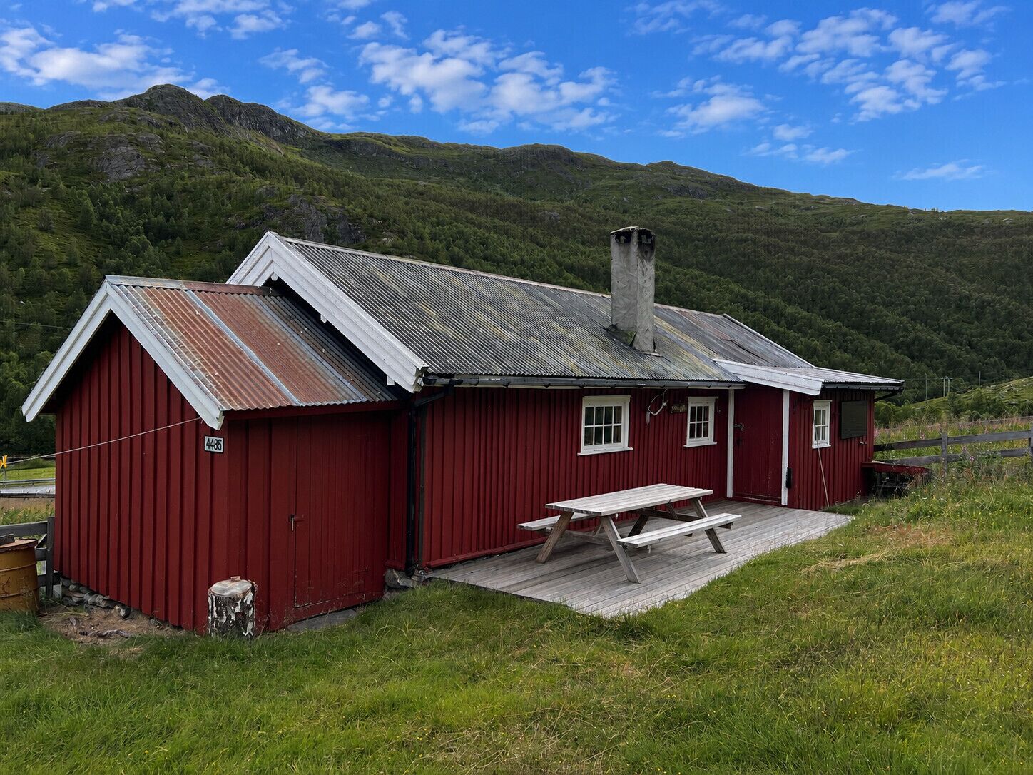 A red wooden building with a metal roof, a picnic table, and a small fenced area.