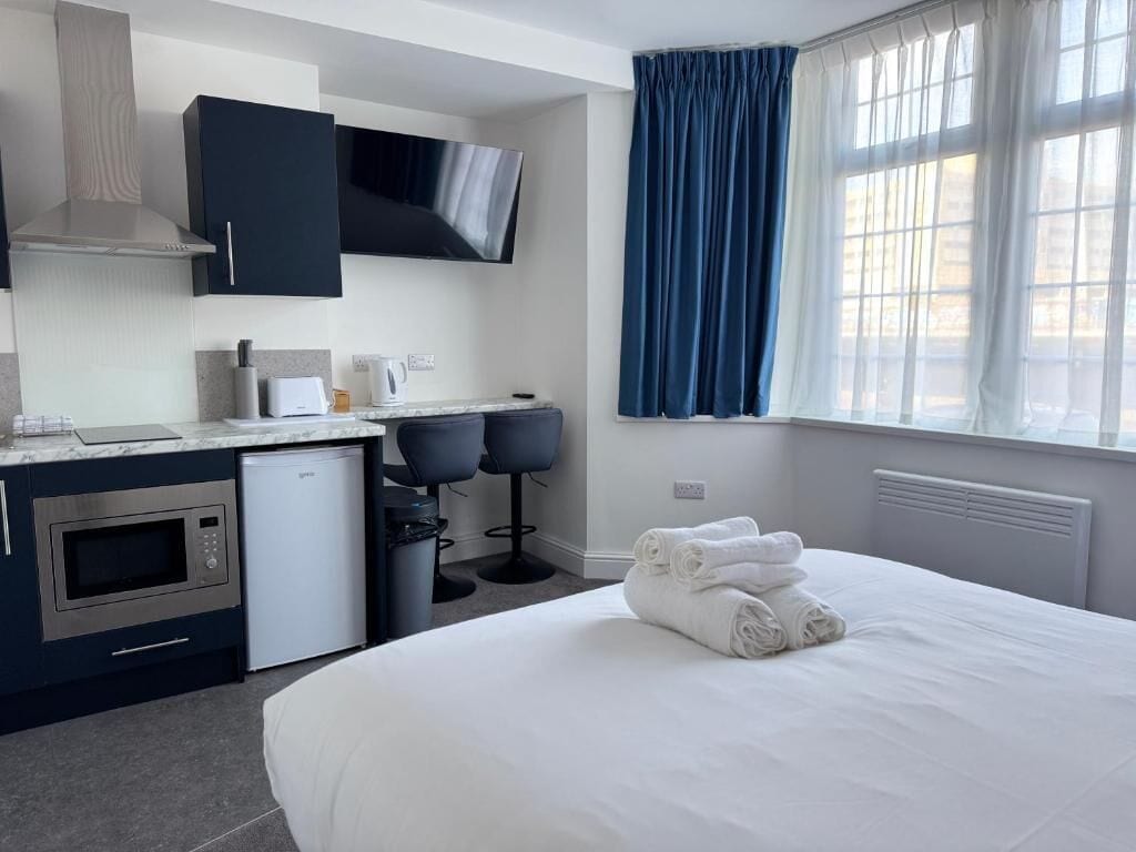 A hotel room with a bed, a desk with a microwave, a coffee machine, and a TV.