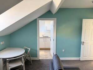 A room with a sloped ceiling, a dining table with chairs, a bench, and a door leading to a kitchen.