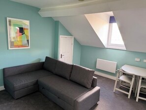 A room with a grey sectional sofa, a white table, and a window with a view.