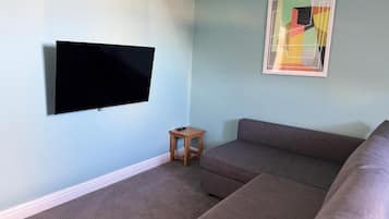 A living room with a flat-screen TV mounted on the wall, a small wooden side table, and a sectional sofa.