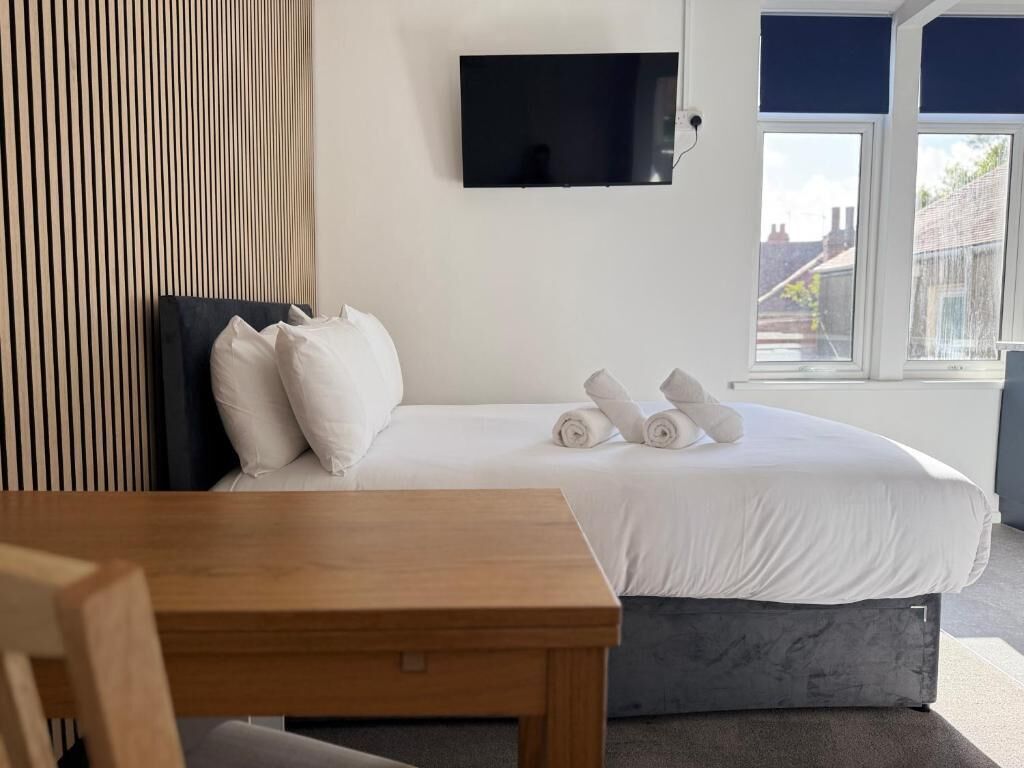 Quarto de hotel com uma cama, televisão na parede e janela com vista para edifícios.