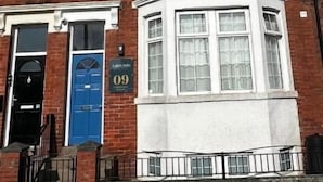 A red brick building with a blue door, numbered 09, and a bay window. - Aaron Wise - 09 Coldstream Studios (Cardiff)