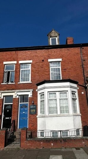 A red brick building with a blue door, numbered 09, and a bay window. - Aaron Wise - 09 Coldstream Studios (Cardiff)