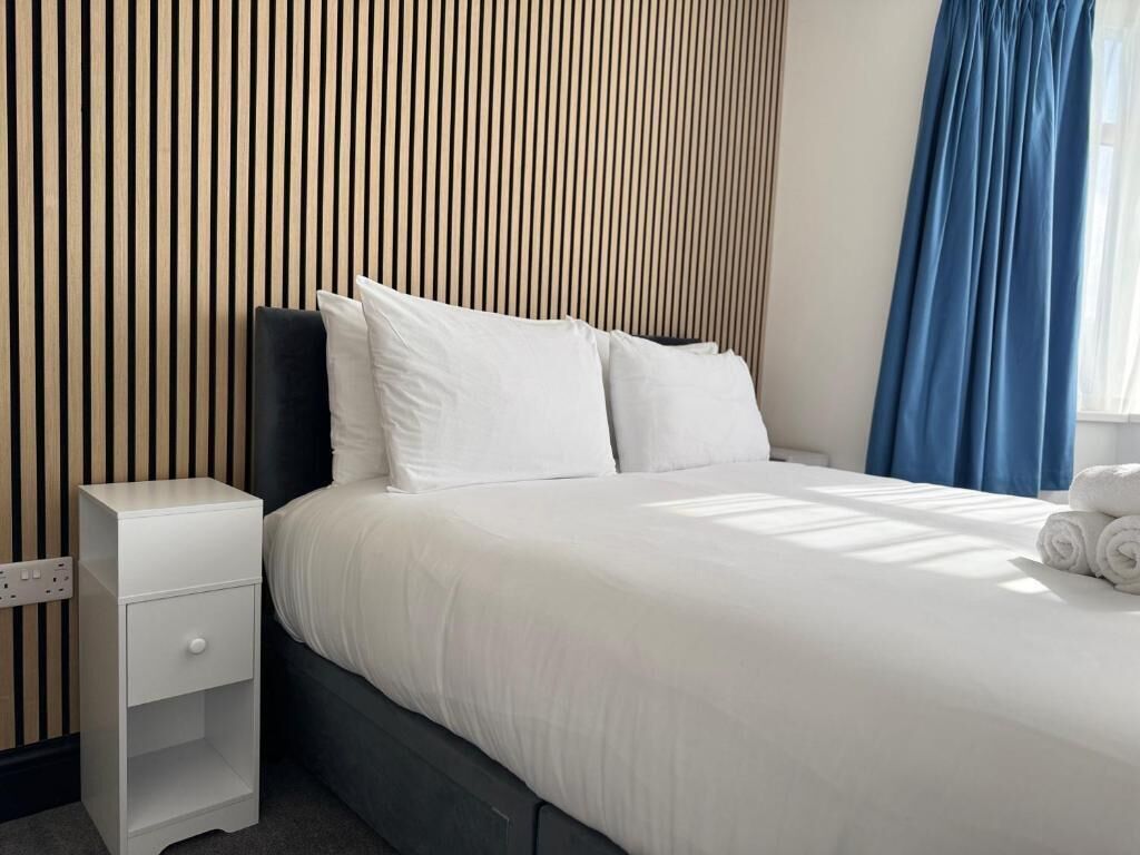 A hotel room with a bed, a nightstand, a wall with vertical lines, and a window with curtains.