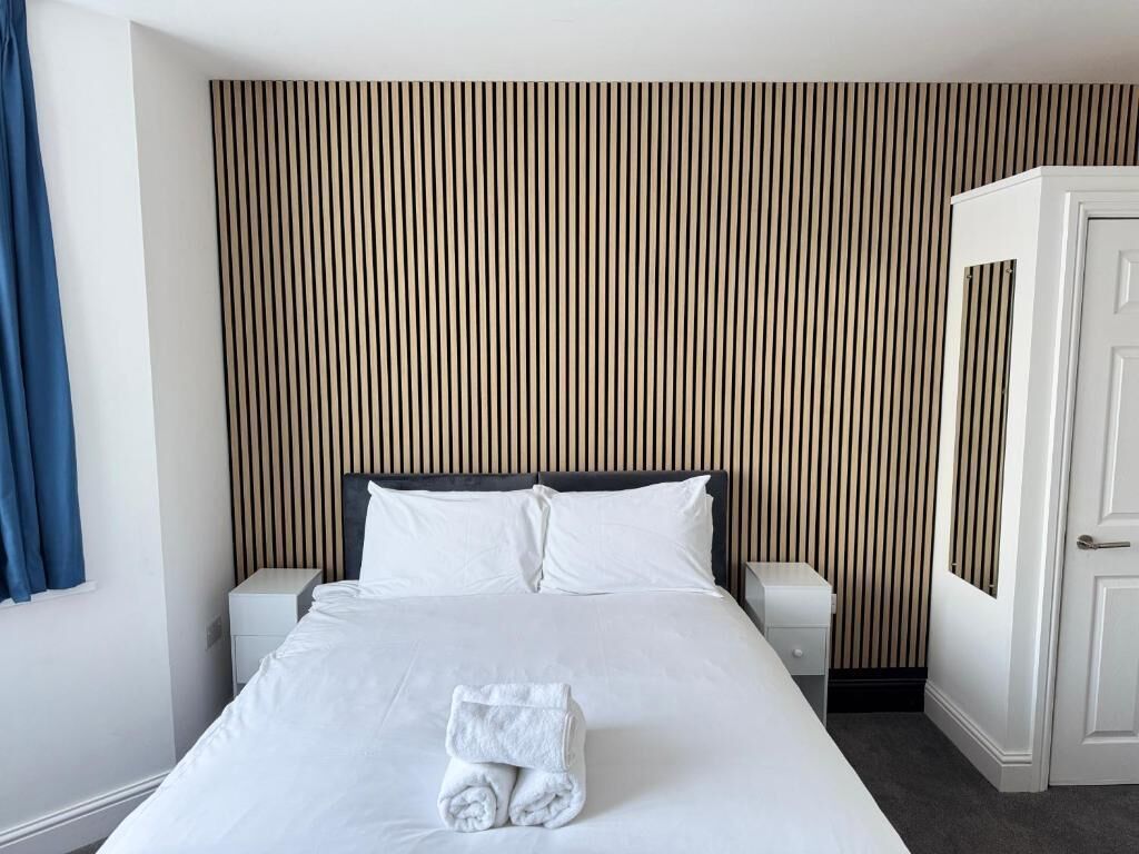 A hotel room with a bed, two bedside tables, a wardrobe, and a striped wall.