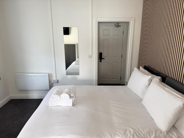 A hotel room with a large bed, a door, a radiator, and a mirror.