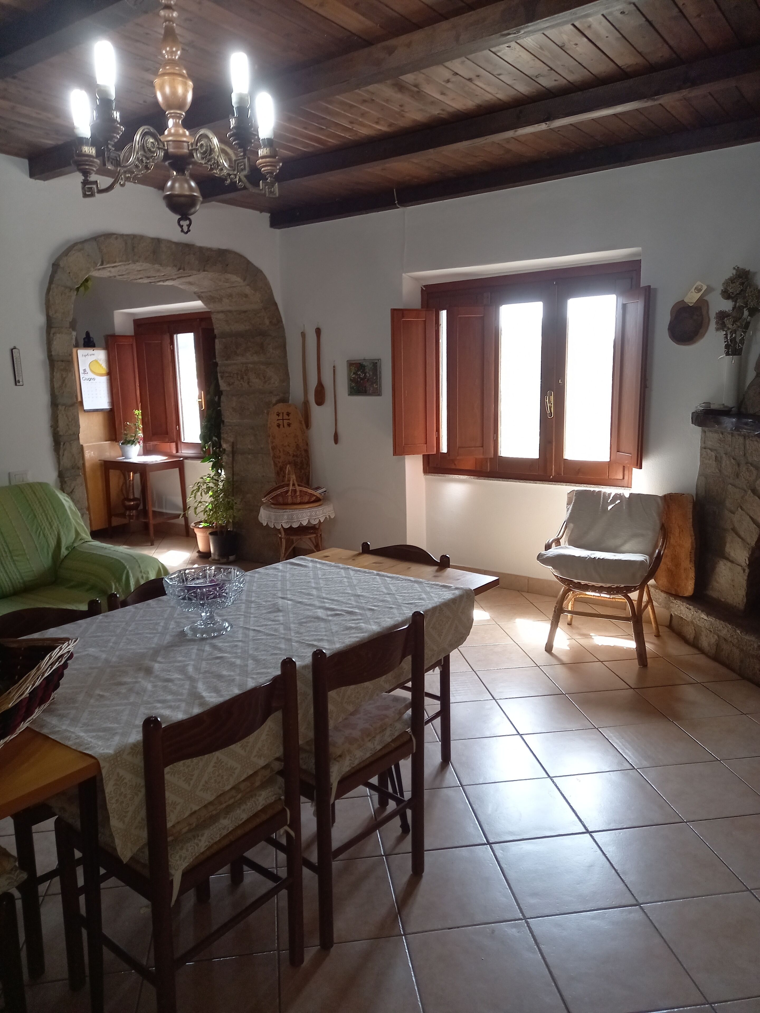 A dining area with a table set for four, wooden chairs, a chandelier, and a stone wall.