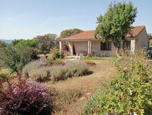 Ein Steinhaus mit Ziegeldach, umgeben von einem Garten mit verschiedenen Pflanzen und Blumen.