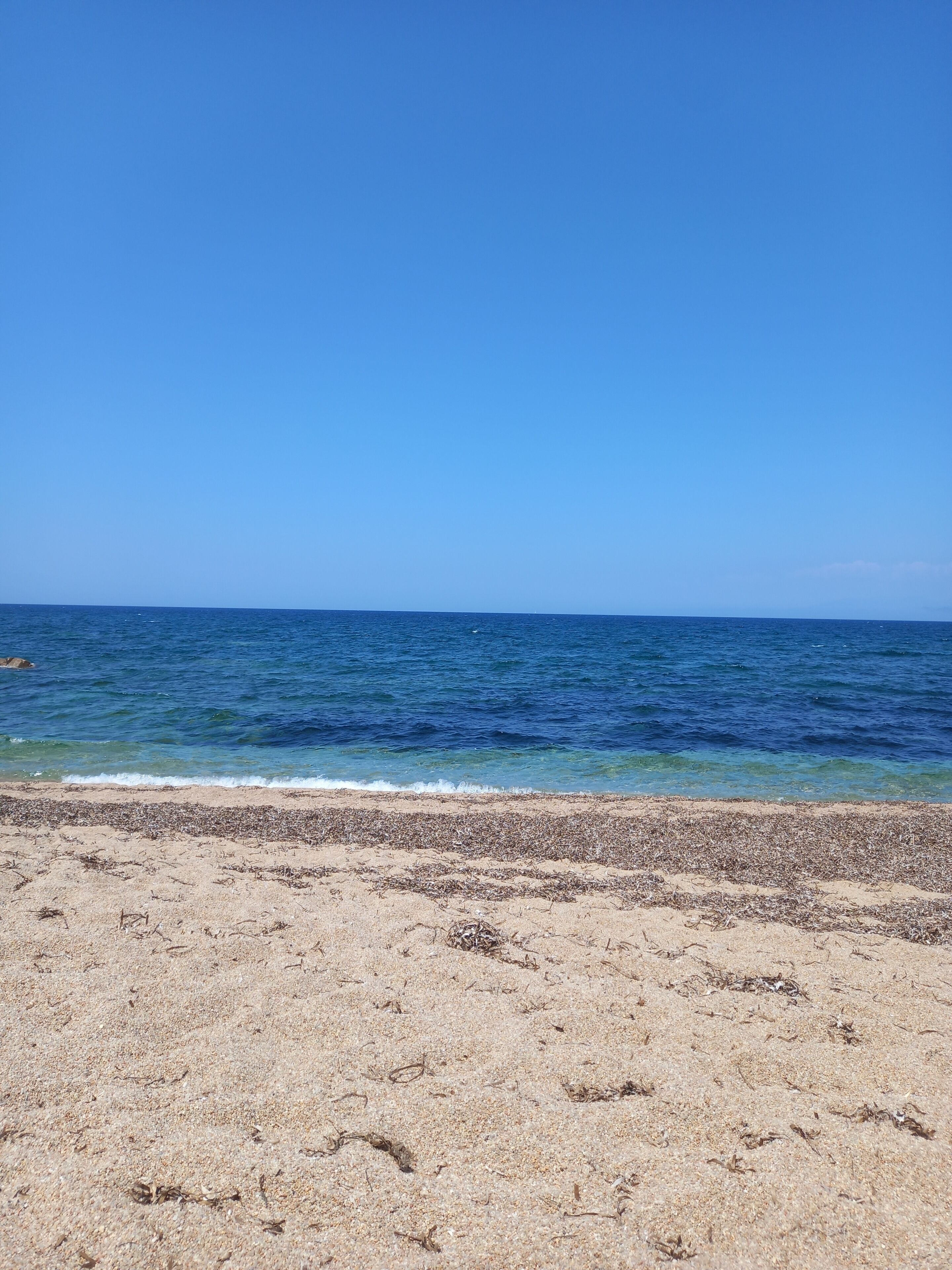 A beach with clear blue water and a sandy shore.