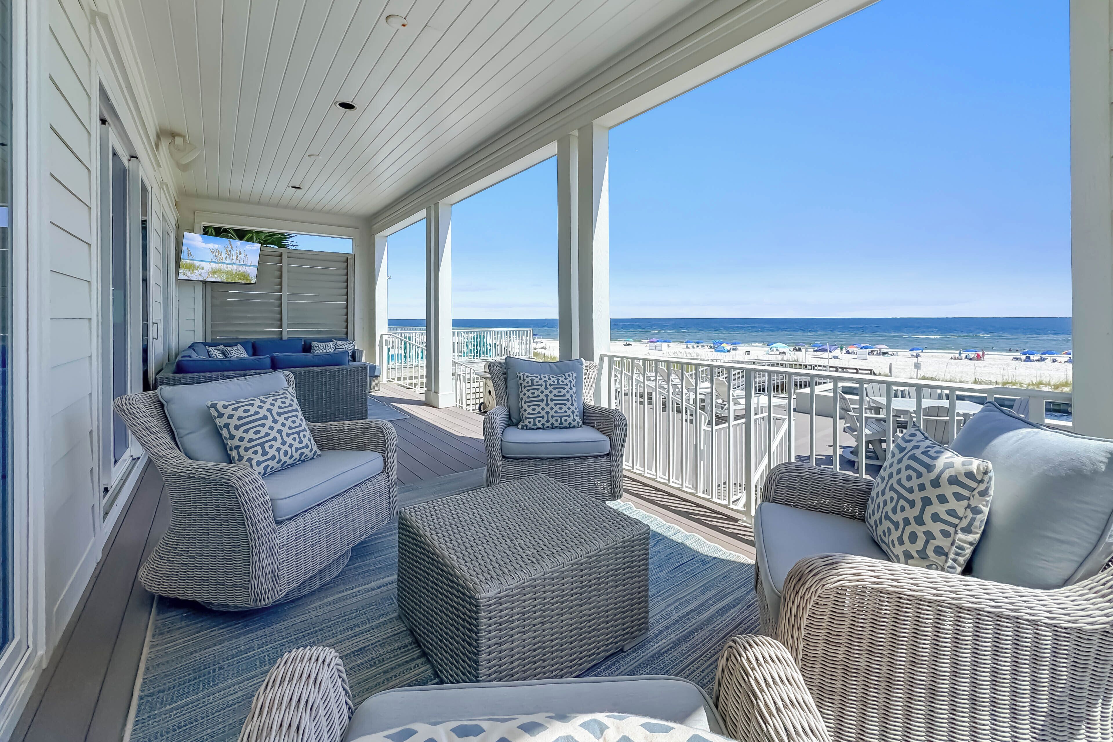 A covered outdoor seating area with wicker furniture and a view of the beach.