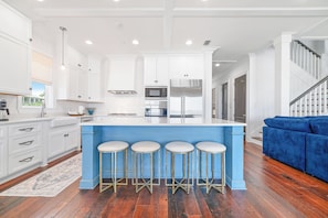 Une cuisine moderne avec des meubles blancs, un îlot central bleu doté de tabourets, des appareils en acier inoxydable et un plancher en bois.