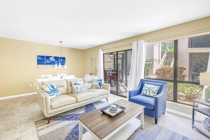 A living room with a sofa, armchair, coffee table, and artwork on the wall. - Gertrude's Siesta | Bayview Unit, Near Beach, Private Patio, Heated Pool, Pickle,Tennis! (Siesta Key)