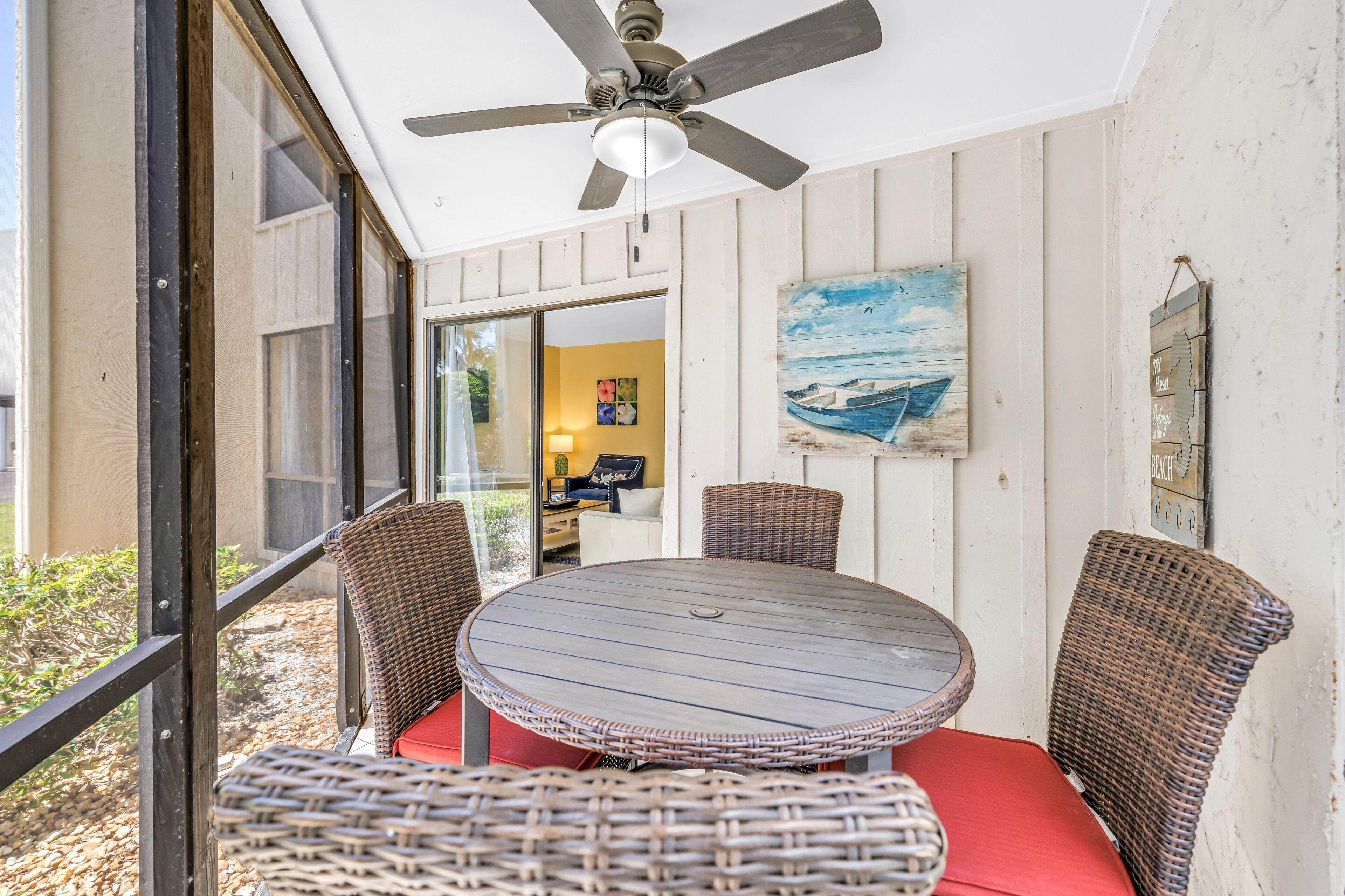 A covered patio with wicker furniture, a ceiling fan, and a painting of a boat.