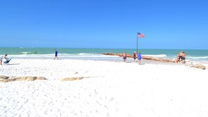 A beach with a sandy shore, a flag, and people walking. - Gertrude's Siesta | Bayview Unit, Near Beach, Private Patio, Heated Pool, Pickle,Tennis! (Siesta Key)