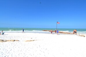 Ein Strand mit sandigem Ufer, einer Flagge und Menschen, die spazieren gehen.