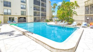 A swimming pool with a tiled deck, surrounded by lounge chairs and palm trees. - Gertrude's Siesta | Bayview Unit, Near Beach, Private Patio, Heated Pool, Pickle,Tennis! (Siesta Key)