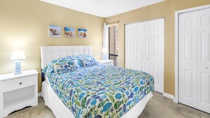 A bedroom with a bed, nightstands, a lamp, a window with curtains, and a door. - Gertrude's Siesta | Bayview Unit, Near Beach, Private Patio, Heated Pool, Pickle,Tennis! (Siesta Key)