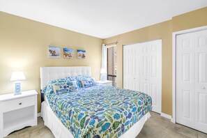 A bedroom with a bed, nightstands, a lamp, a window with curtains, and a door.