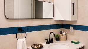 Et badeværelse med en hvid vask, et spejl, en håndklædestang og et toilet.