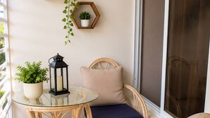 En balkon med fletmøbler, et glasbord og plantekasser.