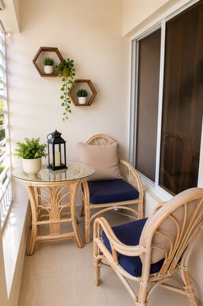A balcony with wicker furniture, a glass table, and potted plants. - Cozy Modern Apartment in La Romana - Close to the Beach (La Romana)