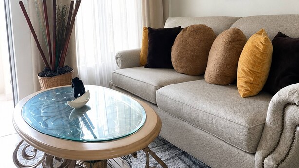 En stue med en beige sofa, et glasbord og en potteplante.