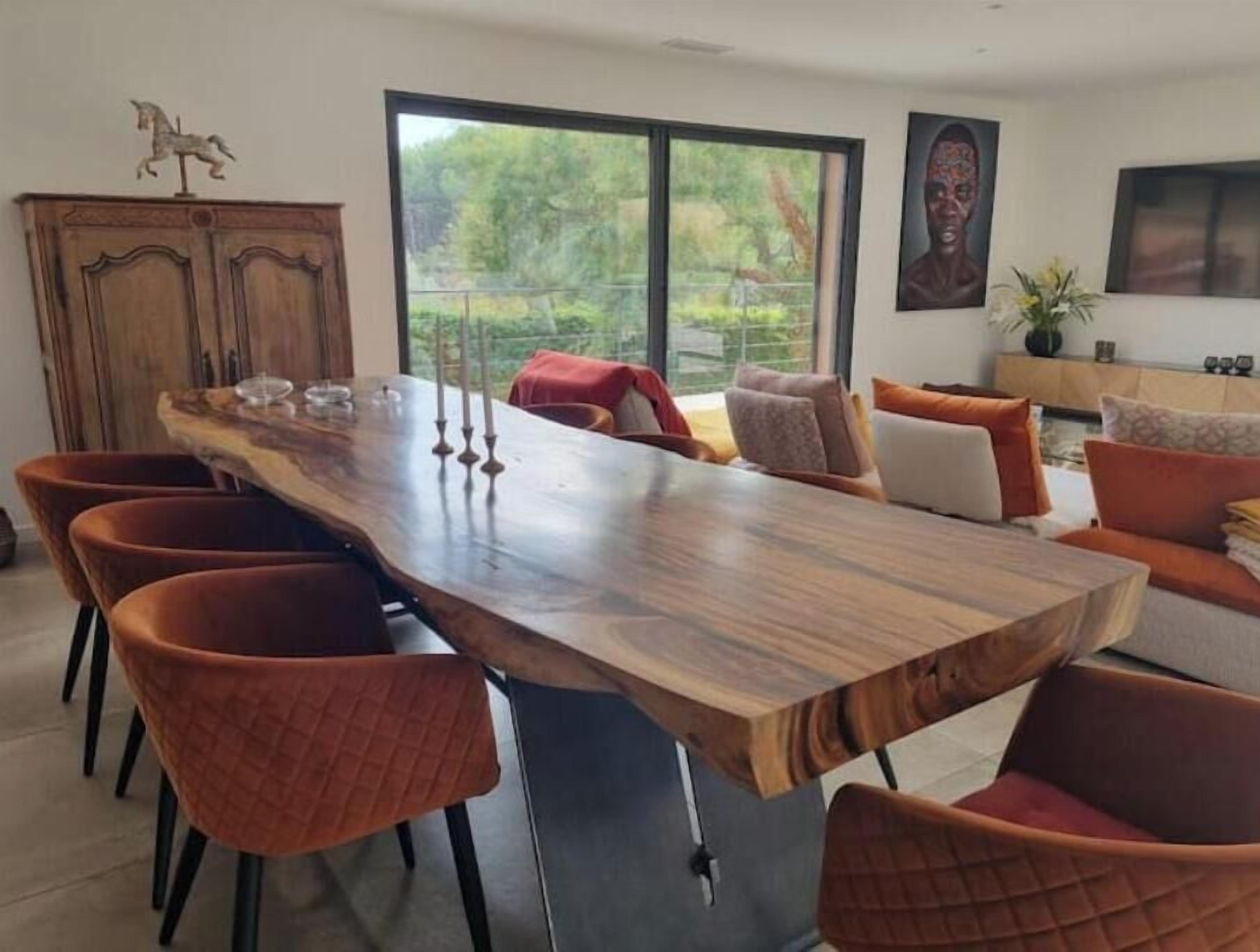 Un comedor con una larga mesa de madera, seis sillas y vistas a zonas verdes.