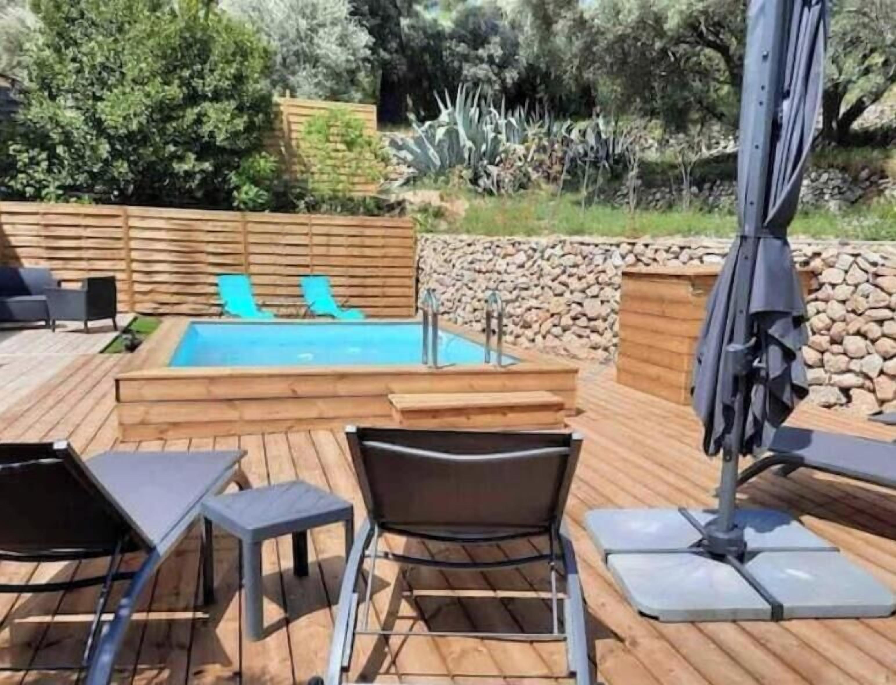 Terraza de madera con piscina, sillones de descanso y una mesa.