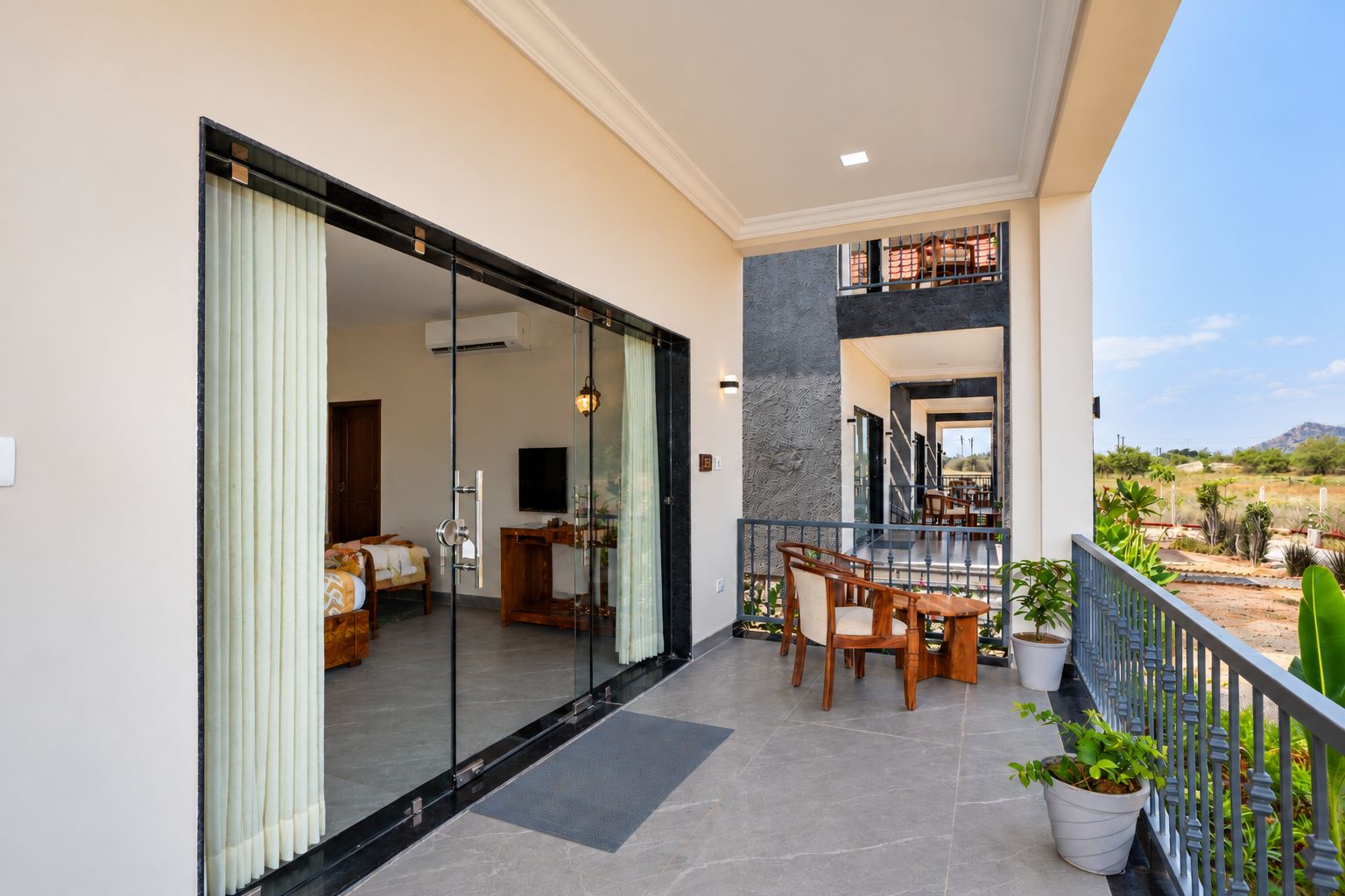 A modern hotel room with a sliding glass door leading to a balcony with a dining area and a view of the landscape.