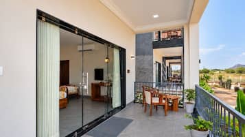 A modern hotel room with a sliding glass door leading to a balcony with a dining area and a view of the landscape.