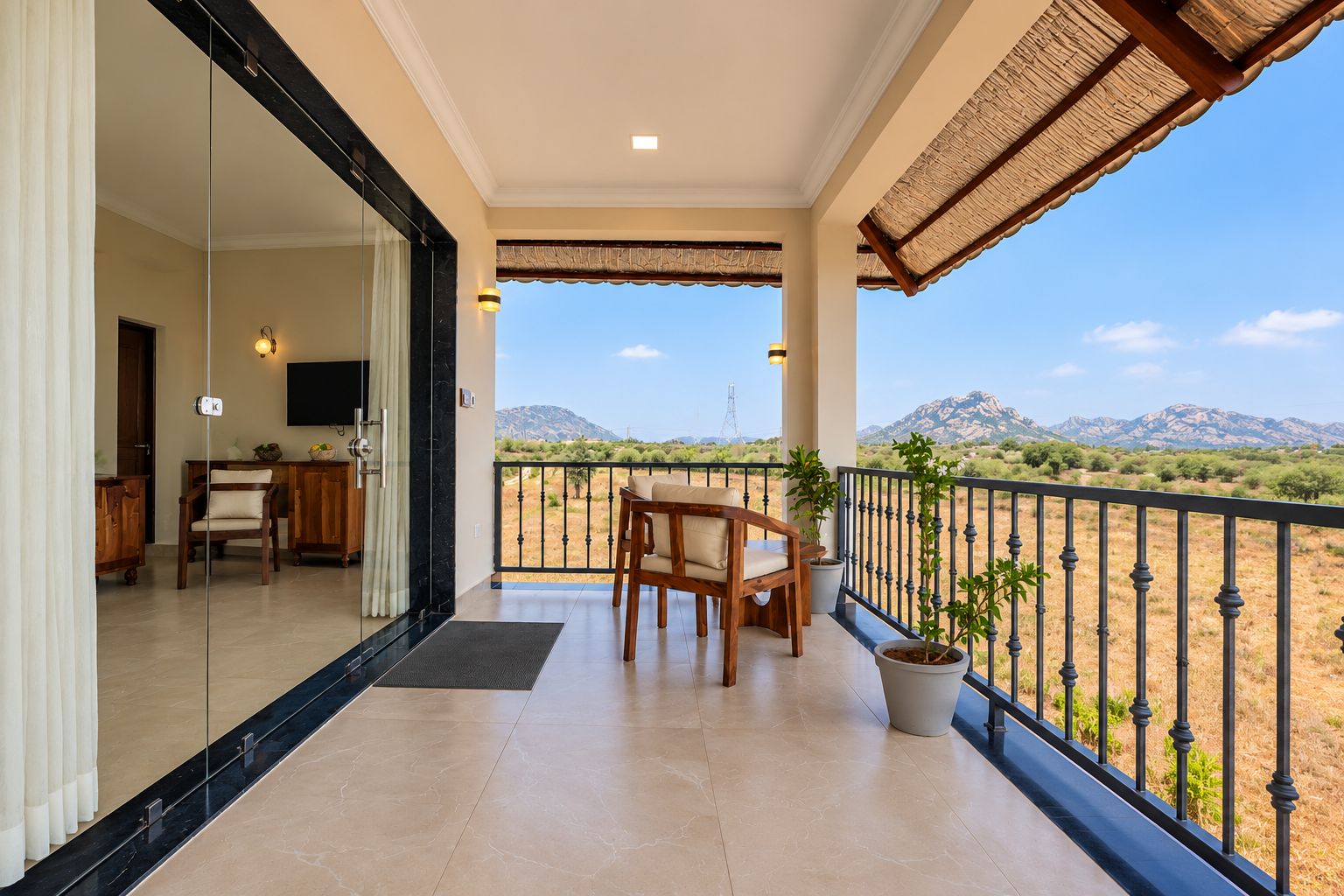 A balcony with a view of a mountainous landscape, a dining area with chairs, and a potted plant.