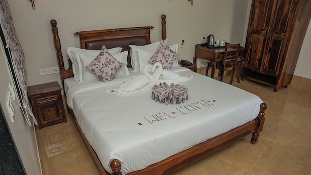 Een net opgemaakt bed met een 'WELCOME' bord, een houten hoofdbord, een nachtkastje en een garderobe.